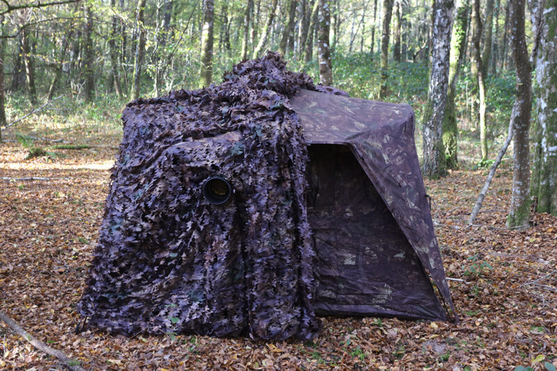 pixelpenguin- Een camouflagenettent verborgen in het bos.