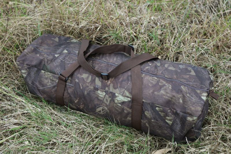 pixelpenguin- Een camouflage plunjezak, die lijkt op een Tragopan Monal 2-persoons Schuiltent, ligt discreet in het dikke gras.