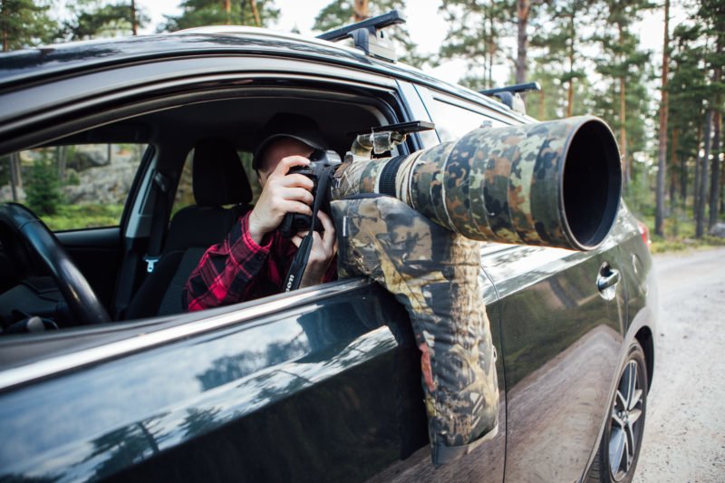 pixelpenguin- Een man maakt heimelijk een foto met zijn gecamoufleerde camera in zijn auto, waarbij hij de tweepotige zitzak gebruikt voor stabiliteit.