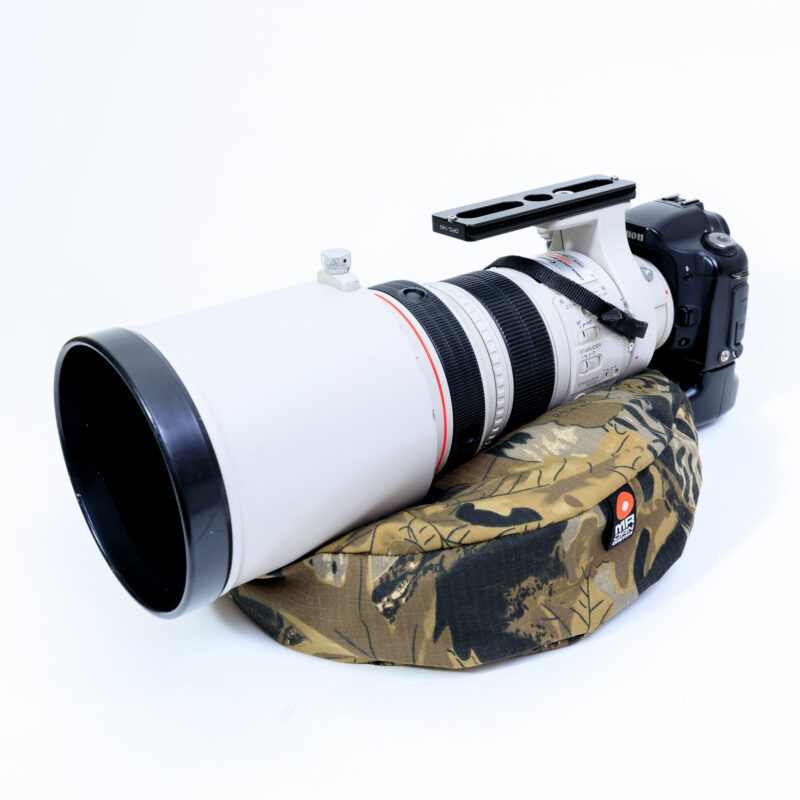 pixelpenguin- Een cameralens zit bovenop een camouflagehoes, ondersteund door een Big Drum Bean Bag.