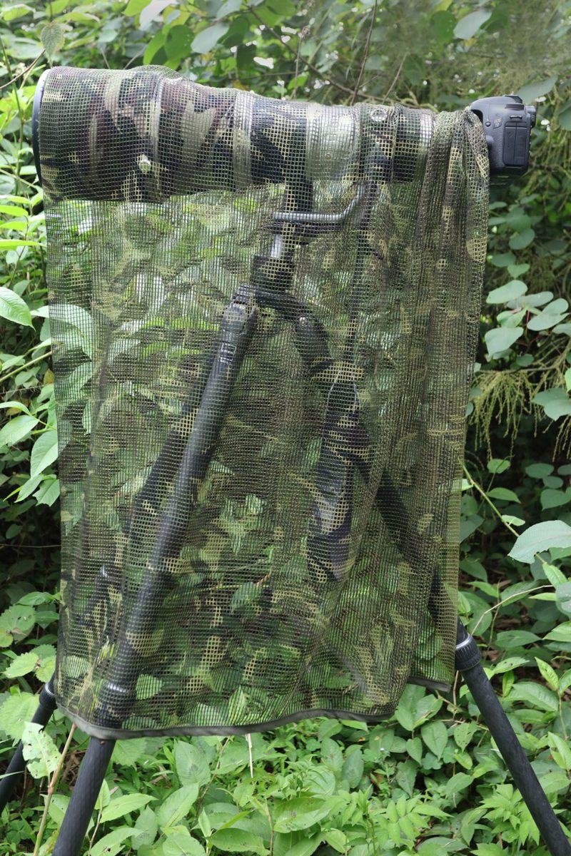 pixelpenguin- Een Camouflage das-spotting scope op een statief in het bos, die uitstekende mogelijkheden biedt voor het ongestoord observeren van dieren in het wild.