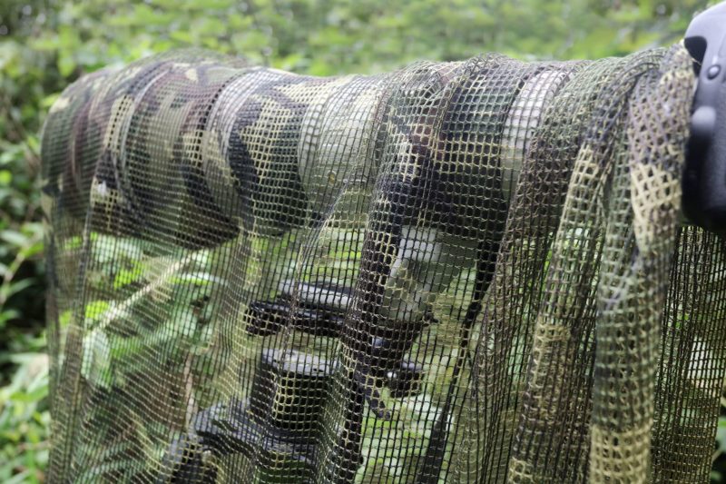 pixelpenguin- In het bos wordt een camouflagenet aan een paal bevestigd, waardoor een verborgen camouflagedas ontstaat.
