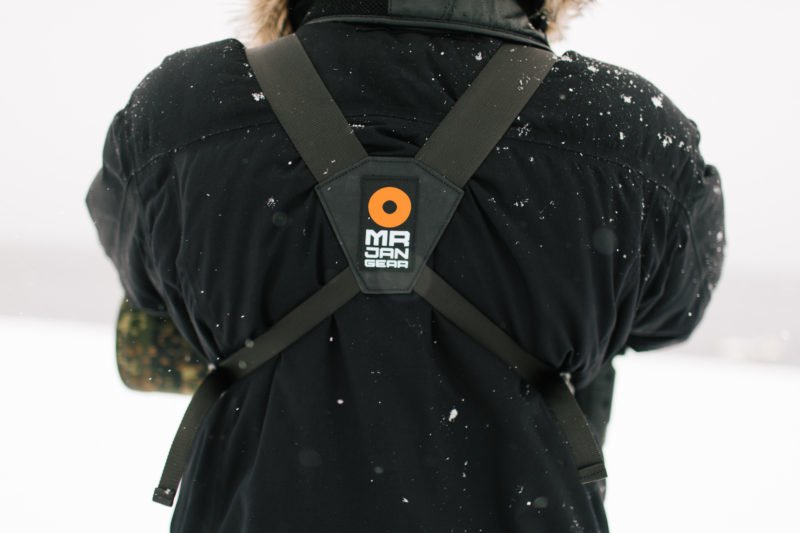 pixelpenguin- De rug van een persoon die een harnas draagt in de sneeuw terwijl hij een lensdrager draagt.