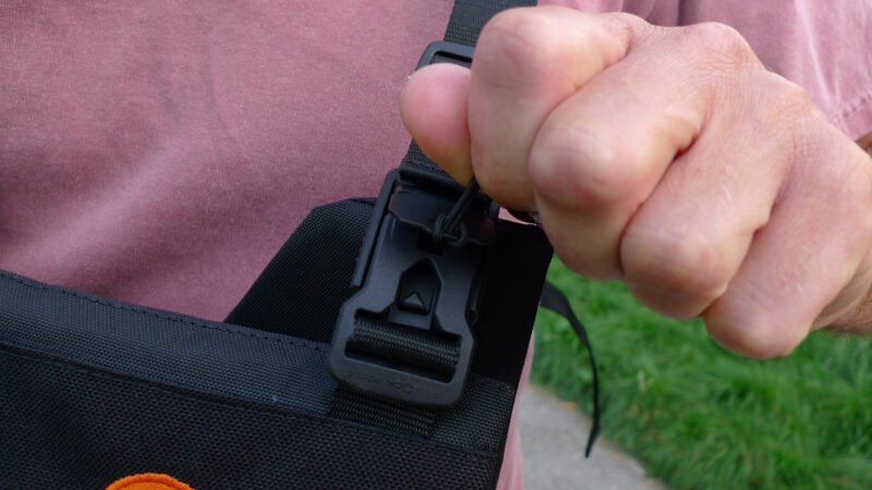 A hand opening the FidLock magnetic closure on a MrJan Gear Lens Carrier